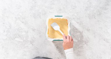 Düz yatıyordu. Şekerli mısır şekeri hazırlamak için parşömen kağıdıyla kaplanmış kare cam fırın tavasına şekerleme dökülüyor..