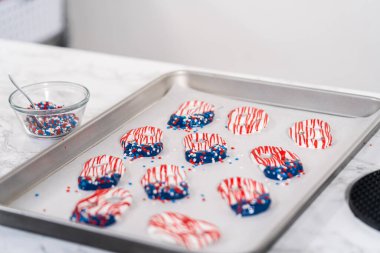 Dipping pretzels twists into melted chocolate to make red, white, and blue chocolate-covered pretzel twists.