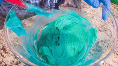 İyi ışıklandırılmış bir mutfakta, yeşil ve diğer renklerin çeşitli tonlarında tereyağlı krema çeşitleri büyüleyici kapkeklerin sanatsal dekorasyonu için titizlikle karıştırılıyor ve hazırlanıyor.