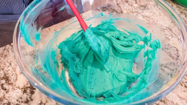 İyi ışıklandırılmış bir mutfakta, yeşil ve diğer renklerin çeşitli tonlarında tereyağlı krema çeşitleri büyüleyici kapkeklerin sanatsal dekorasyonu için titizlikle karıştırılıyor ve hazırlanıyor.