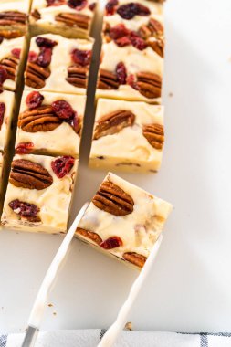 Beyaz çikolatalı fındıklı fındıklı şekerlemeyi beyaz bir kesme tahtasında küçük parçalara ayırmak..