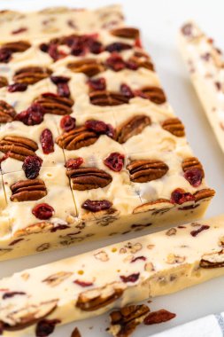 Beyaz çikolatalı fındıklı fındıklı şekerlemeyi beyaz bir kesme tahtasında küçük parçalara ayırmak..