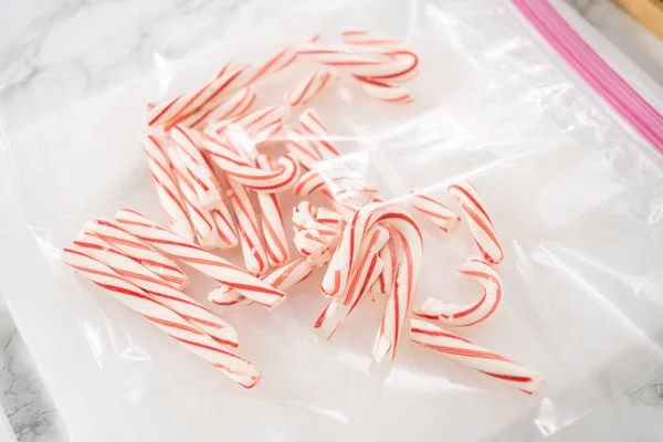 Crushing peppermint candies in a plastic bag with a marble rolling pin on a white cutting board.