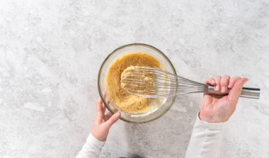 Flat lay. Mixing ingredients with a hand whisk in a large mixing bowl to bake banana cookies with chocolate drizzle.