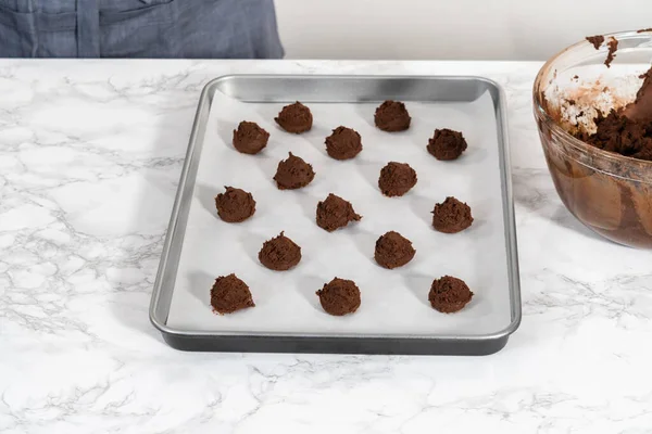 Scooping cookie dough with dough scoop into a baking sheet lined with parchment paper to bake chocolate cookies with chocolate hearts for Valentines Day.
