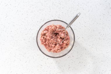 Flat lay. Mixing ingredients with a potatoe masher in a glass mixing bowl to prepare oven-baked meatballs.