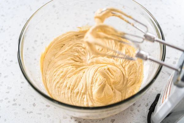 Mixing ingredients with a hand mixer in a large mixing bowl to bake dulce de leche cupcakes.