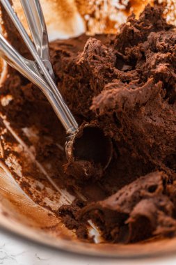 Scooping cookie dough with dough scoop into a baking sheet lined with parchment paper to bake chocolate cookies with chocolate hearts for Valentines Day.