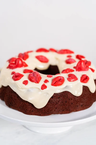 Freshly baked red velvet bundt cake with chocolate lips and hearts over cream cheese glaze for Valentines Day.