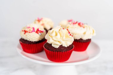 Taze pişmiş kadife kekler, üzerine beyaz çikolata ganache süslemesi serpilmiş..