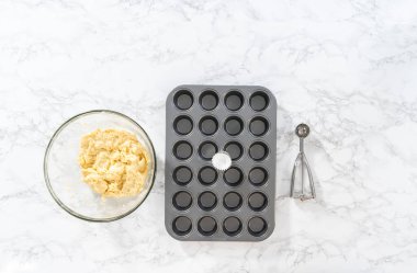 Flat lay. Scooping cupcake batter with dough scoop into a baking cupcake pan with liners to bake mini vanilla cupcakes with ombre pink buttercream frosting.