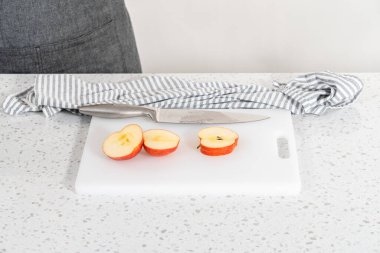 Kırmızı elmaları beyaz bir kesme tahtasının üzerinde ince dilimlere ayırmak.