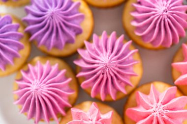 Beyaz pasta standında pembe tereyağlı taze pişmiş mini vanilyalı kekler..