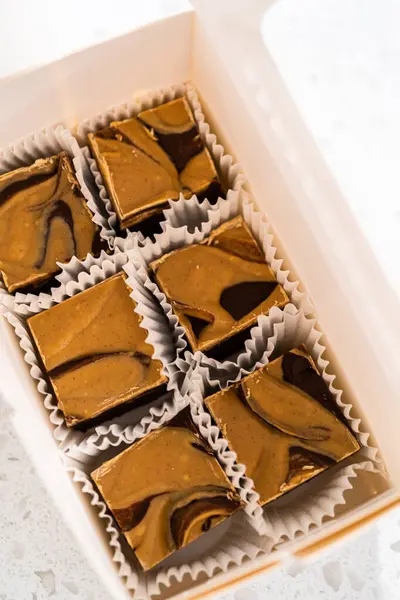 Packaging homemade chocolate fudge with peanut butter swirl into a white gift box.