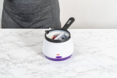 Melting chocolate chips in a candy melting pot to make red, white, and blue chocolate-covered pretzel twists.