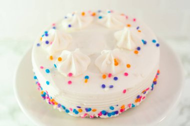 Beyaz kek tabağına funfetti serpiştirilmiş küçük beyaz doğum günü pastası.