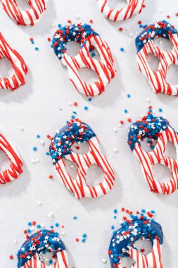 Dipping pretzels twists into melted chocolate to make red, white, and blue chocolate-covered pretzel twists.