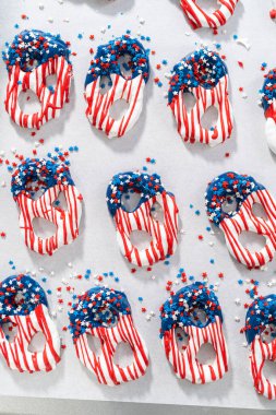 Dipping pretzels twists into melted chocolate to make red, white, and blue chocolate-covered pretzel twists.