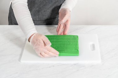 Büyük bir mutfak bıçağıyla yeşil şekerlemeyi beyaz bir kesme tahtasında kare parçalara ayırmak..