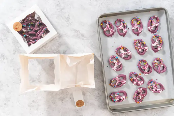 Flat lay. Packaging homemade mermaid pretzel twists into a white paper box.