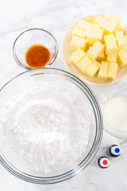 Amerikan bayrağı mini kekleri için tereyağlı krema yapmak için cam karıştırma kaselerinde ölçülmüş malzemeler..