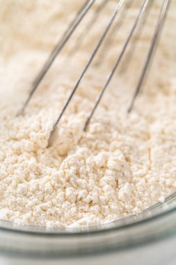 Beyaz çikolatalı macadamia fındığı pişirmek için bardakta çırpma kabıyla kurutulmuş malzemeleri karıştırıyorum..