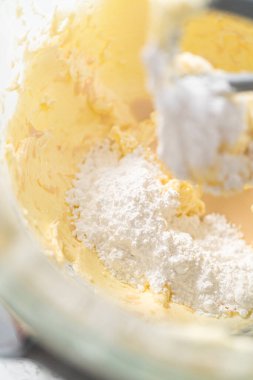 Whisking buttercream frosting in a glass mixing bowl with an electric kitchen mixer for American flag mini cupcakes.