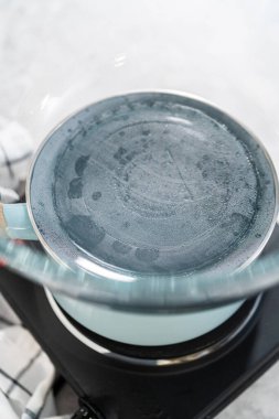 Beyaz çikolata parçacıkları ve diğer malzemeleri kaynayan suyun üzerine karıştırıp çikolatalı macadamia şekerlemesi hazırlıyorum..