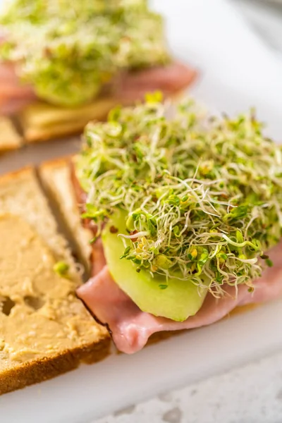 Assembling Ham Cucumber Sprout Sandwiches White Cutting Board — Stock Photo, Image