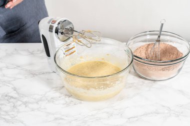 Büyük bir bardakta ıslak malzemeler karıştırarak kırmızı kadife kekler ve beyaz çikolatalı ganache kreması pişiriyorum..