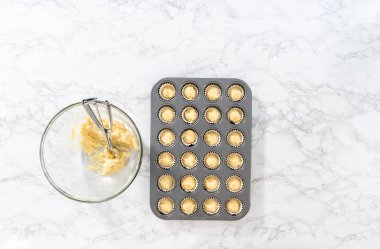 Flat lay. Scooping cupcake batter with dough scoop into a baking cupcake pan with liners to bake mini vanilla cupcakes with ombre pink buttercream frosting.
