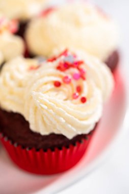 Taze pişmiş kadife kekler, üzerine beyaz çikolata ganache süslemesi serpilmiş..