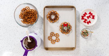 Flat lay. Dipping pretzels twists into melted chocolate to make a chocolate pretzel Christmas wreath.