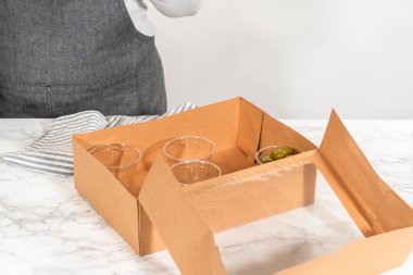 Kurulum sürecinde, bir kadın bu şarküteri kutusunu ustalıkla düzenliyor, dilimlenmiş et, peynir, kraker ve üzüm sergiliyor, hepsi düzgünce düzenlenmiş ve kahverengi bir hediye kutusunda paketlenmiş..