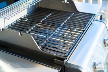 Yakından bakıldığında, banliyödeki bir evin balkonunda ilk açık hava yemek pişirme macerasını bekleyen iki ocaklı ızgaranın bozulmamış ızgarasını gösteriyor..