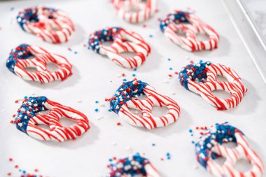 Dipping pretzels twists into melted chocolate to make red, white, and blue chocolate-covered pretzel twists.