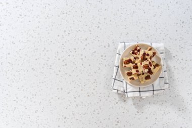 Düz yatıyordu. Beyaz seramik tabakta ev yapımı beyaz çikolatalı fındıklı şekerleme parçaları..