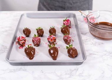 Çikolata kaplı çilekleri hazırlamak için erimiş çikolataya çilek bandırıyorum..