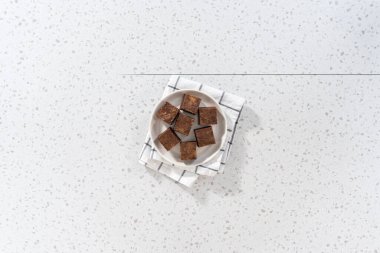 Düz yatıyordu. Beyaz seramik tabakta ev yapımı çikolatalı fıstık ezmeli şekerleme parçaları..