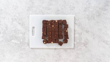 Düz yatıyordu. Büyük bir mutfak bıçağıyla çikolatalı macadamia şekerlemesini beyaz bir kesme tahtasında kare parçalara ayırmak..