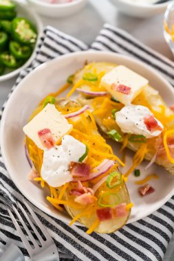 Pressure Cooker Baked Potatoes. Garnished large baked potatoes with butter, sour cream, cheese, and bacon bits on a white plate.