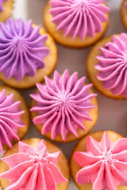 Beyaz pasta standında pembe tereyağlı taze pişmiş mini vanilyalı kekler..