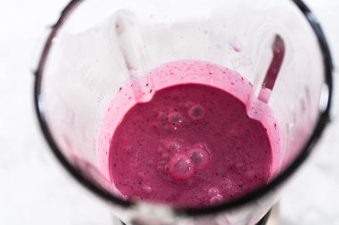 Mixing ingredients in kitchen blender to prepare mixed berry boba smoothie.