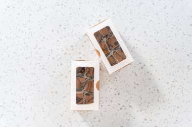 Düz yatıyordu. Fıstık ezmeli ev yapımı çikolatalı şekerlemeler beyaz bir hediye kutusuna konuyor..