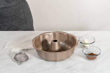 Greasing metal bundt cake pan with vegetable shortening and cocoa powder to bake gingerbread bundt cake with caramel filling.