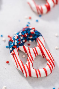Dipping pretzels twists into melted chocolate to make red, white, and blue chocolate-covered pretzel twists.