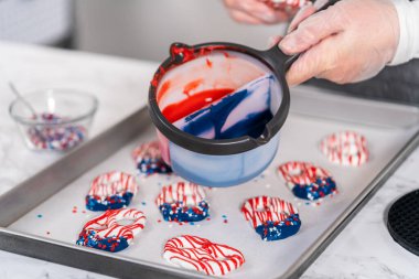 Dipping pretzels twists into melted chocolate to make red, white, and blue chocolate-covered pretzel twists.