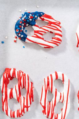 Dipping pretzels twists into melted chocolate to make red, white, and blue chocolate-covered pretzel twists.