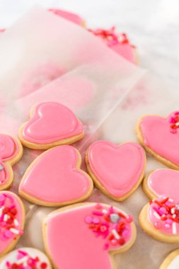 Kalp şeklinde şeker kurabiyelerini büyük plastik bir kapta pembe ve beyaz kraliyet kreması ile depolamak.