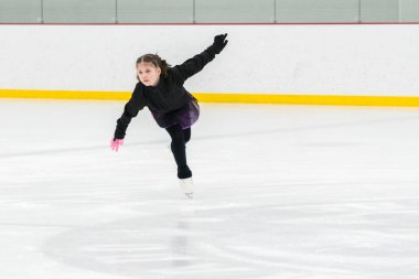 Artistik patinaj rutinini mükemmelleştiren genç bir kız kapalı bir buz pateni sahasında yarışma elbisesini giyerken.